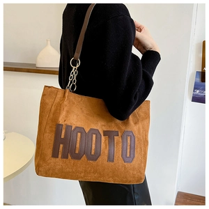 Detail view of large brown suede tote bag with HOOTO patch and chain strap worn by model