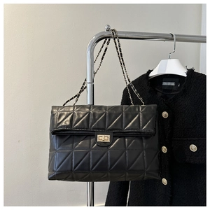 Detail of black quilted shoulder bag with gold turn-lock closure and chain strap