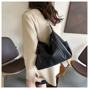 Detail view of a large black leather tote bag with multiple metal zippers on a beige blazer