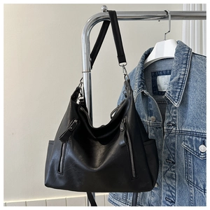 Detail of black soft leather tote bag with vertical zippers and side pockets on denim jacket