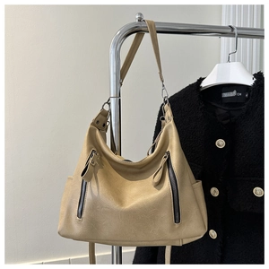 Detail of khaki leather tote bag with vertical zippers and adjustable strap on a stand