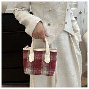 Detail of red and grey plaid wool bucket bag with cream leather handles and gold hardware