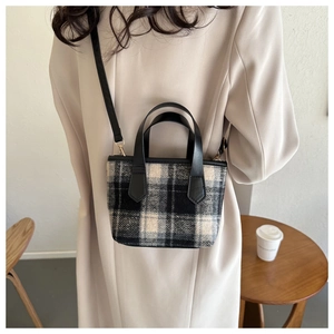 Plaid tweed tote bag with leather handles and gold buckles worn as a crossbody bag