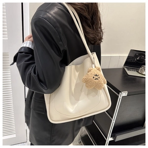 Detail of creamy white tote bag featuring vertical stitching and a brown plush bear charm