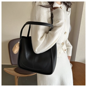 Detail of black matte leather tote bag with brown plush charm and elegant U-shaped stitching