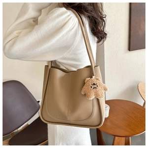 Close-up of a khaki tote bag in synthetic leather featuring a cute plush bear pendant