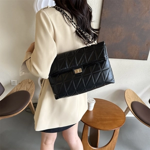 Large black quilted chain shoulder bag with gold hardware worn by a model in a room