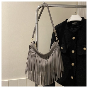 Detail of dark gray suede shoulder bag featuring long fringe and gold metal hardware