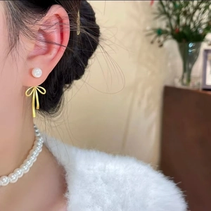 Boucles d'oreilles nœud doré et perle portées par un mannequin au style rétro chic