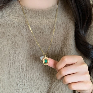 Retro golden necklace with oval emerald green pendant on camel knit sweater
