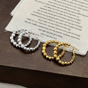 Orecchini a cerchio con perle geometriche oro e argento su sfondo in tessuto vintage