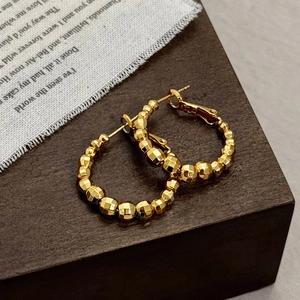 Elegant gold plated hoop earrings with multi-faceted beads on a wooden display