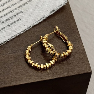 Close-up of golden geometric hoop earrings featuring beaded cube accents on wood surface