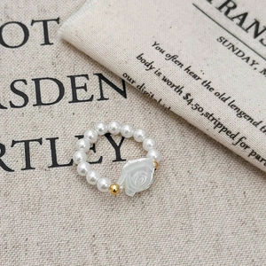 Elegant beaded pearl ring featuring a white rose charm and golden accents on soft fabric