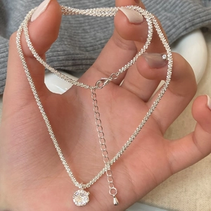 Detail of silver chain necklace with a sparkling round zircon pendant held by hand