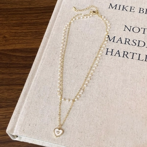 Close-up of double-layer necklace with white pearls, gold chain and heart pendant