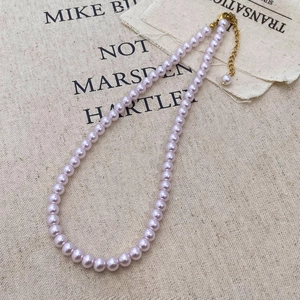 Detail view of light purple pearl necklace with golden lobster clasp on textured beige fabric
