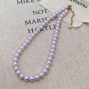 Macro shot of taro purple pearl necklace with golden lobster clasp on rustic linen