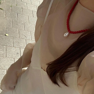 Detail of red beaded necklace featuring a white teardrop pearl pendant on a model