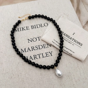 Close-up of black beaded necklace with a white teardrop pearl pendant on linen cloth
