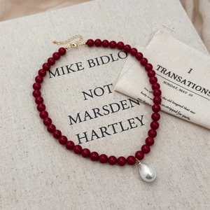 Close-up of red beaded necklace featuring a white teardrop pearl pendant on canvas