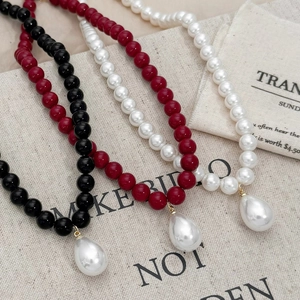 Beaded necklaces in black, red, and white with teardrop pearl pendants on beige linen