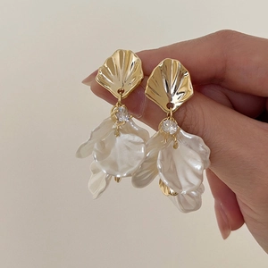 Macro detail of fan-shaped gold earrings with zircon and pearly white petals