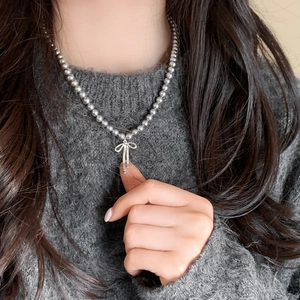 Elegant grey pearl necklace featuring a silver bow pendant worn on a grey knit sweater