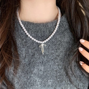 Elegant purple pearl necklace with a silver bow pendant worn over a grey sweater