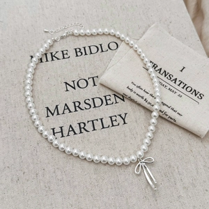 Detail of elegant pearl necklace featuring a silver bow pendant on a beige linen background