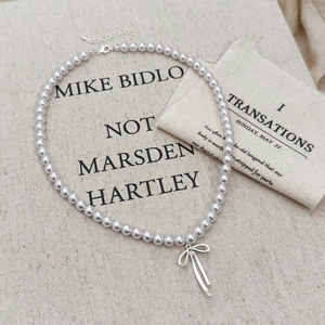 Macro detail of pearl necklace with silver bow pendant on textured linen fabric