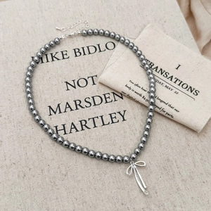 Close-up of dark grey pearls necklace with a silver ribbon bow pendant on fabric