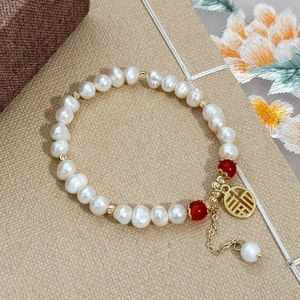 Bracelet en perles baroques avec perles rouges et pendentif doré Fu sur fond textile