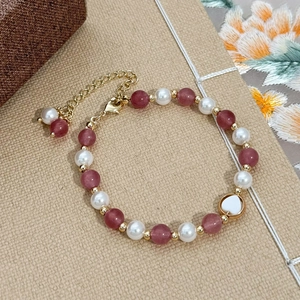 Pink strawberry crystal and pearl beaded bracelet with a gold heart pendant on soft texture