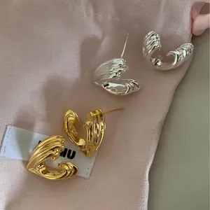 Close-up of gold and silver C-shaped earrings with ripple texture on pink fabric