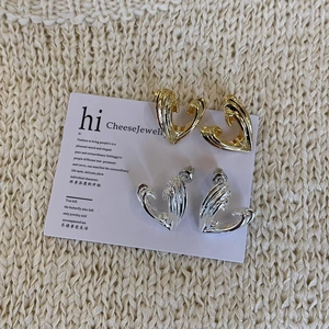 Macro detail of abstract heart-shaped stud earrings in gold and silver mirror finish