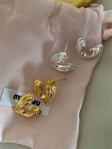 Detail shot of twisted gold and silver C-shaped hoop earrings on a soft velvet pouch