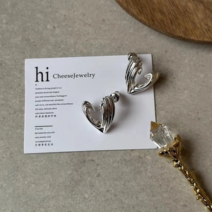 Macro view of silver heart earrings with wavy 3D metallic texture on stone backdrop