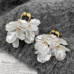 Detailed view of pearl white floral petal tassel earrings on a textured fabric backdrop