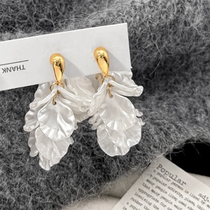 Detail of elegant gold earrings with layered white flower petals on a soft grey fabric