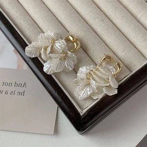 Detail of elegant gold flower earrings with layered white pearlescent petals and tassels