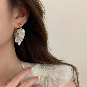 Macro detail of layered white flower petal tassel earrings on model with golden hooks