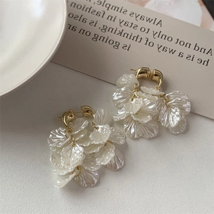 Detail shot of white petal tassel earrings with gold chain on a minimalist stone surface