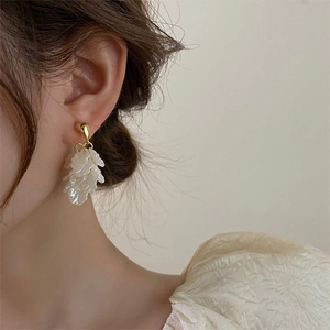Detail of floral petal tassel earrings in gold finish worn by model with soft lighting