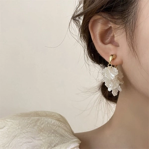 Detail of elegant gold hook earrings with layered white petal pendants on a model