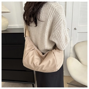 Sac à bandoulière demi-lune en nylon beige avec large sangle porté par le modèle