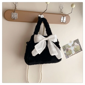 Détail du sac en peluche noir avec un grand nœud blanc et une élégante chaîne de perles