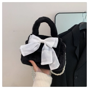 Détail du sac à main noir en peluche avec grand nœud blanc et bandoulière en perles