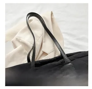 Close-up of black quilted nylon tote bag with leather strap on stylish white background