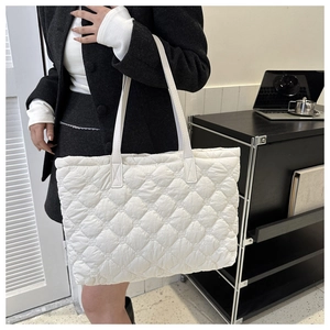 Detail of white quilted tote bag featuring padded diamond patterns and long shoulder straps